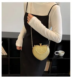 Detailed view of a gold heart-shaped evening bag with a chain strap on a model.