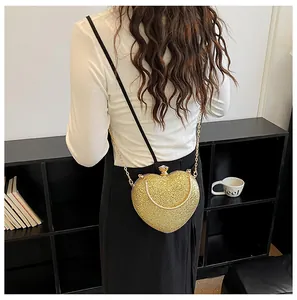 Detail view of a gold heart-shaped evening bag with a chain strap worn by a woman