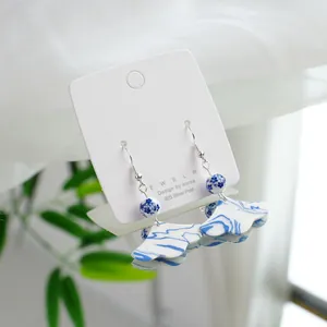 Elegant blue and white porcelain earrings with silver hooks displayed on a white jewelry card.