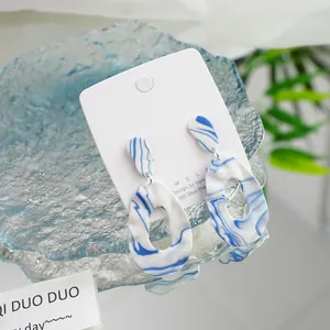 Close-up of blue and white swirl pattern ceramic earrings on a white display card.