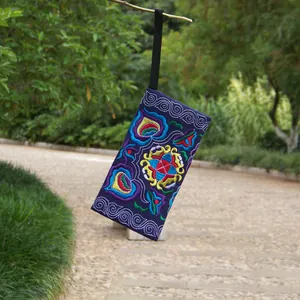 Detail shot of vibrant floral embroidery on a navy blue ethnic style canvas clutch bag.