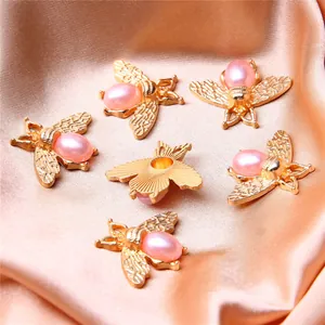Close-up of golden alloy bee pendants with pink pearls for DIY jewelry making