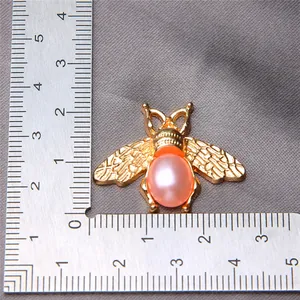 Detailed view of alloy bee pendant with pink pearl body next to a ruler for scale
