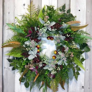 Lush artificial greenery wreath featuring ferns and berries against a rustic wooden background
