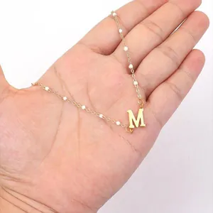 Minimalist gold letter M pendant necklace with elegant white pearl chain accents.