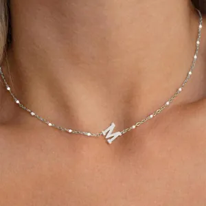Close-up of silver initial M pendant on a dainty pearl-embellished chain necklace.