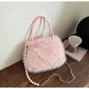 Minimalist pink faux fur handbag with pearl and gold chain strap on a wooden table.