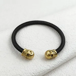Gothic C-shaped twisted cable bracelet with double golden skull heads on white textured background