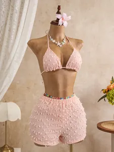 Dettaglio del set bikini rosa testurizzato con top a lupetto e pantaloncini su manichino.