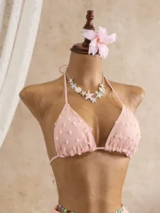 Dettaglio ravvicinato di un top bikini rosa testurizzato con delicate decorazioni a frange
