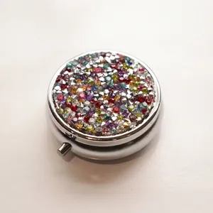 Portable round metal pill box featuring a sparkling colorful rhinestone lid in silver finish