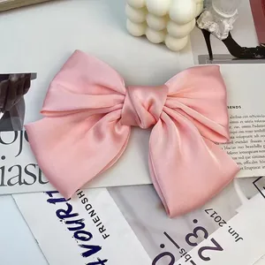 Detailed close-up of a pink satin oversized bow hair clip on a decorative magazine background
