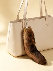 Detailed view of a large fluffy fox tail fur keychain pendant hanging on a beige leather bag