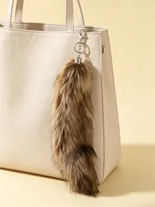 Close-up of extra large fluffy fox tail keychain hanging on a stylish beige handbag