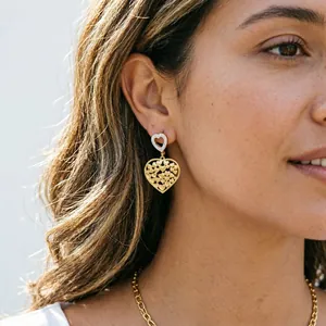Primo piano di orecchini a cuore in acciaio dorato indossati da una modella.