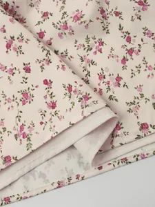 Detailed view of the small pink floral print and neat hem stitching on a light beige dress.