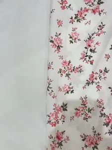Gros plan sur un tissu blanc léger avec des motifs floraux roses et des feuilles vertes.