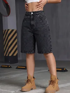 Detail of high-waisted washed black denim shorts paired with tan boots in urban setting