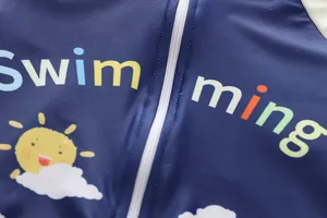 Detailaufnahme des Kinderbadeanzugs mit Swimming-Aufdruck und weißem Reißverschluss