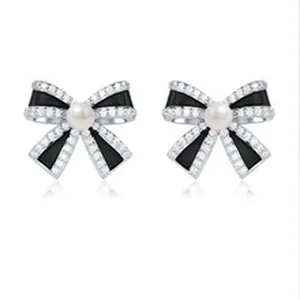 Close-up of elegant S925 silver bow stud earrings featuring pearls and black enamel details
