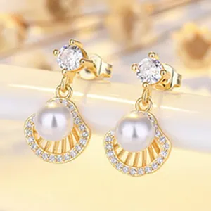 Macro view of elegant gold-plated seashell earrings with pearl and crystal details.