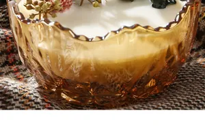 Detailed macro view of high-end scented candle in amber fluted glass jar with floral accents