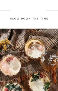 Close-up of scented candles in amber glass jars with dried flower decorations on a blanket.