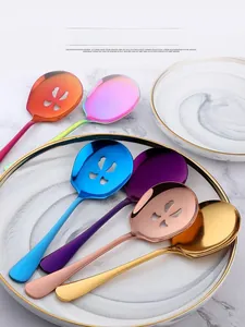 Cucchiai da portata colorati in acciaio inox su eleganti piatti di ceramica bianca.