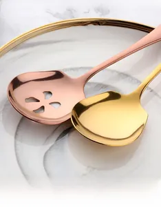 Primo piano di cucchiai da portata in acciaio inossidabile oro e oro rosa su piatto.
