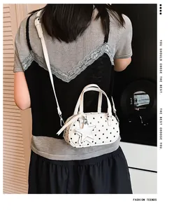 White polka dot bowling handbag with star charm detail shown on a model's shoulder.
