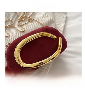 Nahaufnahme einer burgunderroten Wildleder-Clutch mit auffälligem goldfarbenem C-Metallgriff