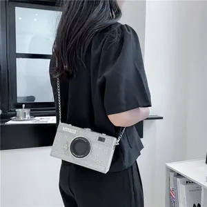 Detail shot of a creative silver camera-shaped crossbody box bag worn by a model.