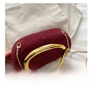 Detail einer burgunderfarbenen Wildleder-Clutch mit großem Goldgriff und Kette
