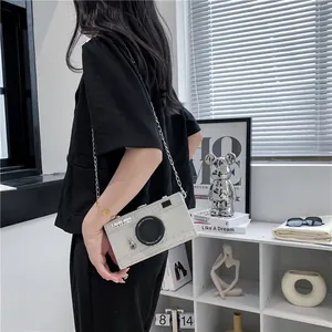 Silver camera-shaped box bag with a delicate silver chain strap shown on a model