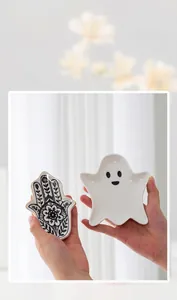 Hand holding ghost and Hamsa hand shaped ceramic jewelry trays for desk organization.