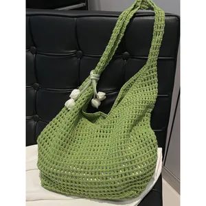 Sac cabas ajouré au crochet vert avec breloques fleurs blanches sur un fauteuil