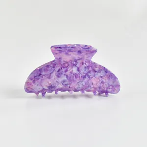 Gros plan d'une pince à cheveux en acétate marbré violet sur fond blanc pur.