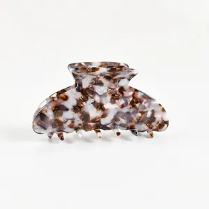 Pince à cheveux en acétate avec motif écaille marron et blanc sur fond neutre blanc.