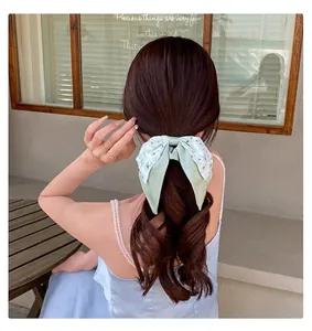 Détail d'un chouchou à fleurs vertes avec rubans de style forêt sur une queue de cheval.