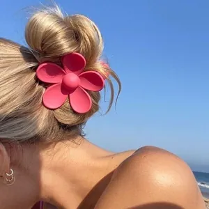 Large matte pink flower hair claw clip accessory shown on a blonde bun against a blue sky