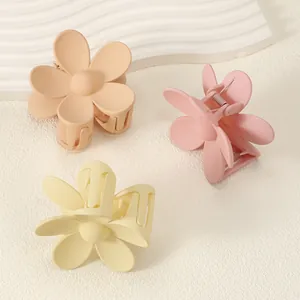 Macro detail of three matte pastel flower hair claws in pink, yellow and orange colors.