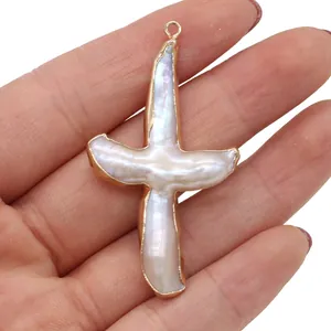 Pendentif en nacre naturelle en forme de croix montrant sa texture bio à la main