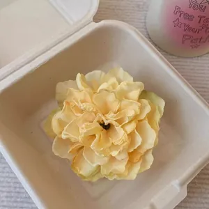Vue détaillée d'une pince à cheveux en forme de pivoine jaune vintage dans un boîtier.