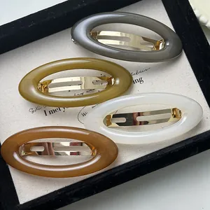 Close-up of four oval acrylic hair clips in earthy colors shown on a stylish display tray.