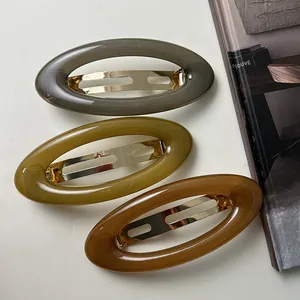 Detail view of three retro acrylic oval hair clips in gray, olive, and brown tones