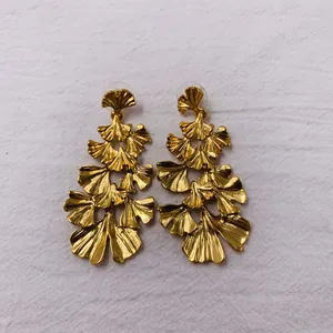 Detailed close-up of vintage gold multi-layered ginkgo leaf statement earrings on fabric.