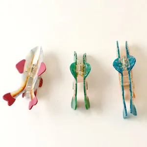 Detail view of three fish-shaped acetate hair claw clips with metallic springs on white.