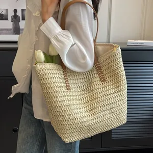 Woven straw tote bag with brown leather straps held by a model in a white shirt