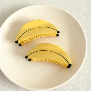 A stylish pair of fun banana-shaped yellow acetate hair claw clips on a white plate
