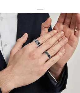 Detailed view of vintage scroll-pattern stainless steel rings on a man's hand wearing a suit